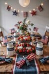 Rustic wooden table decorated for the 4th of July with mason jar centerpieces, red and blue napkins, fresh berries, mini cheesecakes, and small American flags.