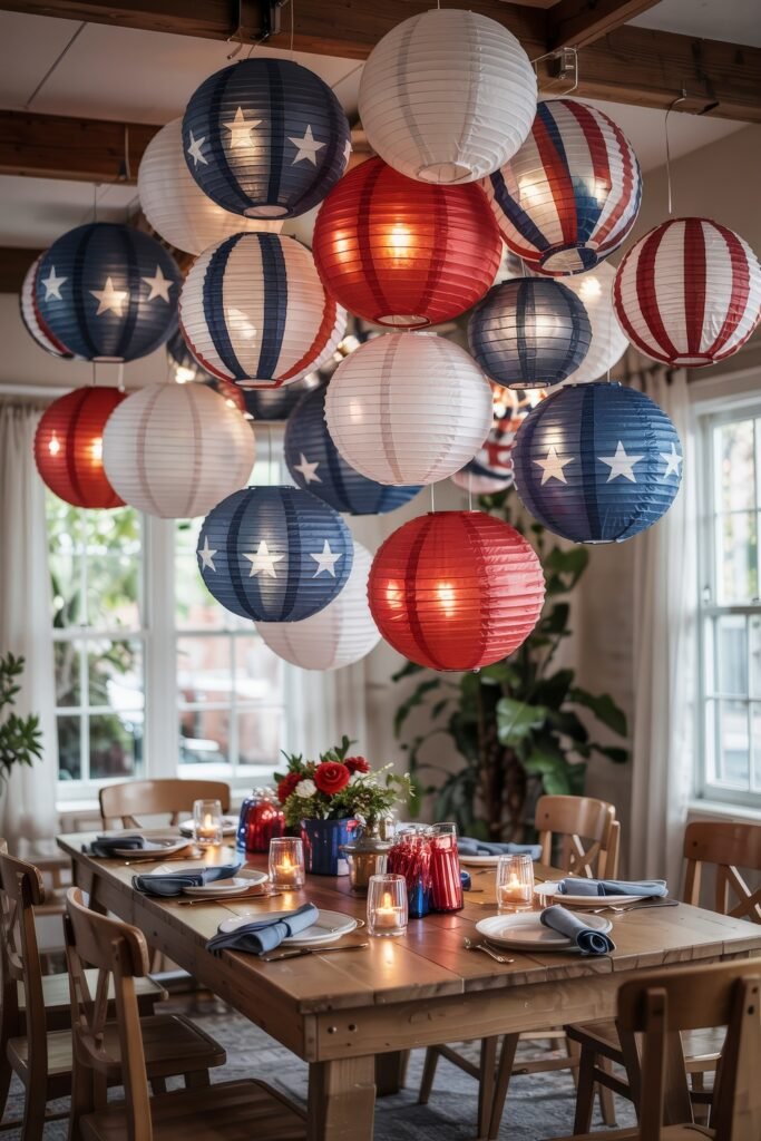 Patriotic 4th of July Table Décor & Centerpieces 19 Dining room decorated with red, white, and blue paper lanterns hanging over a wood table set for a cozy 4th of July gathering.