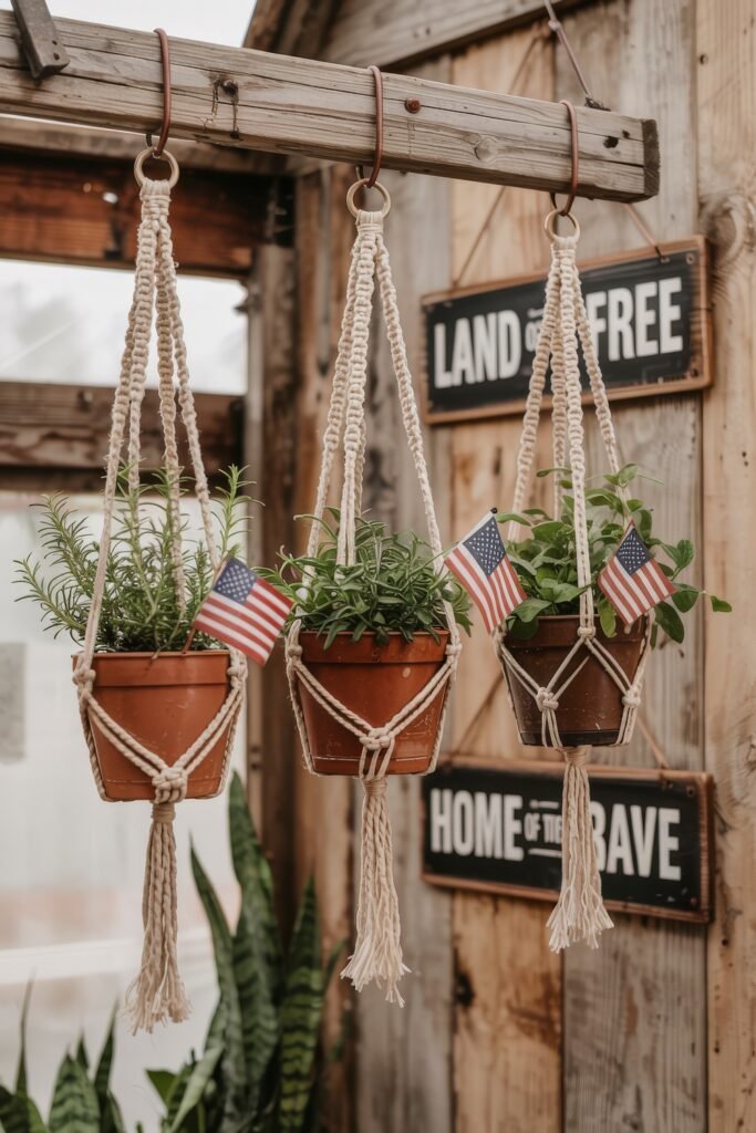 Patriotic 4th of July Table Décor & Centerpieces 23 Rustic patriotic garden display with three hanging macramé planters holding herbs and mini American flags, styled near wood signs reading "Land of the Free" and "Home of the Brave".