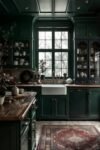 Dark Academia Kitchen Cabinets: Shades & Hardware for a Vintage Aesthetic Snowy window view over a farmhouse sink, surrounded by rich green Dark Academia Kitchen Cabinets and vintage decor.