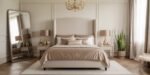 Elegant bedroom with a tall upholstered headboard, beige and taupe bedding, gold accents, twin bedside tables with matching lamps, a large mirror, and a potted plant, capturing a Classy Luxury Master Bedroom aesthetic.