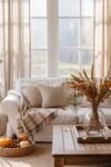 Cozy white sofa with knitted pillows, plaid throw, and fall decorations in a bright sunroom.