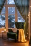 Cozy Fall Sunroom Ideas: Autumn Decor for a Warm Retreat Cozy green armchair with a chunky knit blanket and lantern in a wintery sunroom with fairy lights.