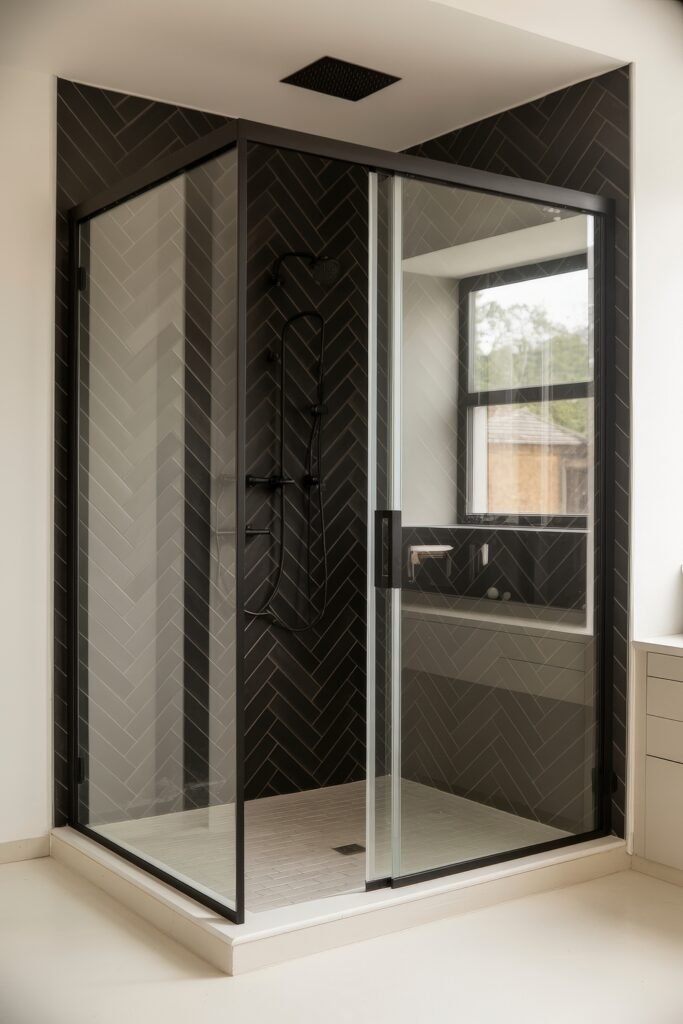 Black Bathroom Ideas: Genius Ways to Create Moody Glam 21 Contemporary glass shower enclosure with black herringbone tile walls, matte black rain showerhead, and white tiled floor, blending contrast and symmetry in Black Bathroom Ideas.