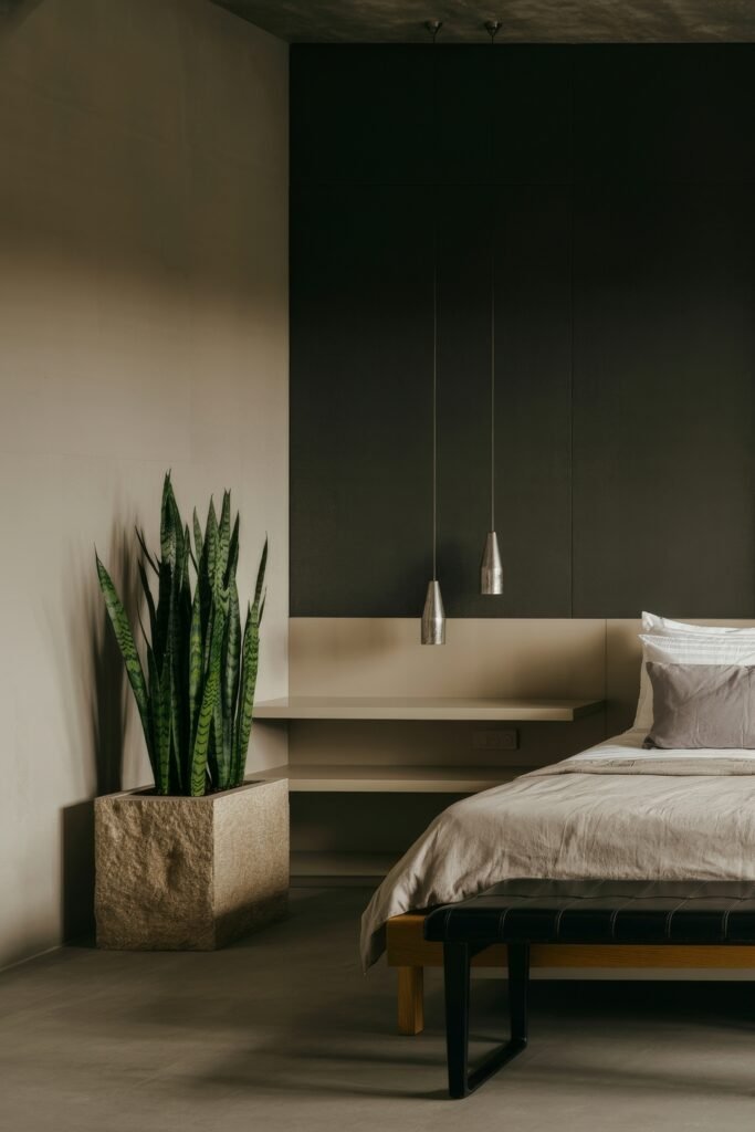 Masculine Luxury Bedroom: Genius Luxe Ideas 31 Minimalist bedroom with earthy tones, a dark accent wall, neutral bedding, and a tall snake plant in a rough stone planter adding height and greenery to the serene space.
