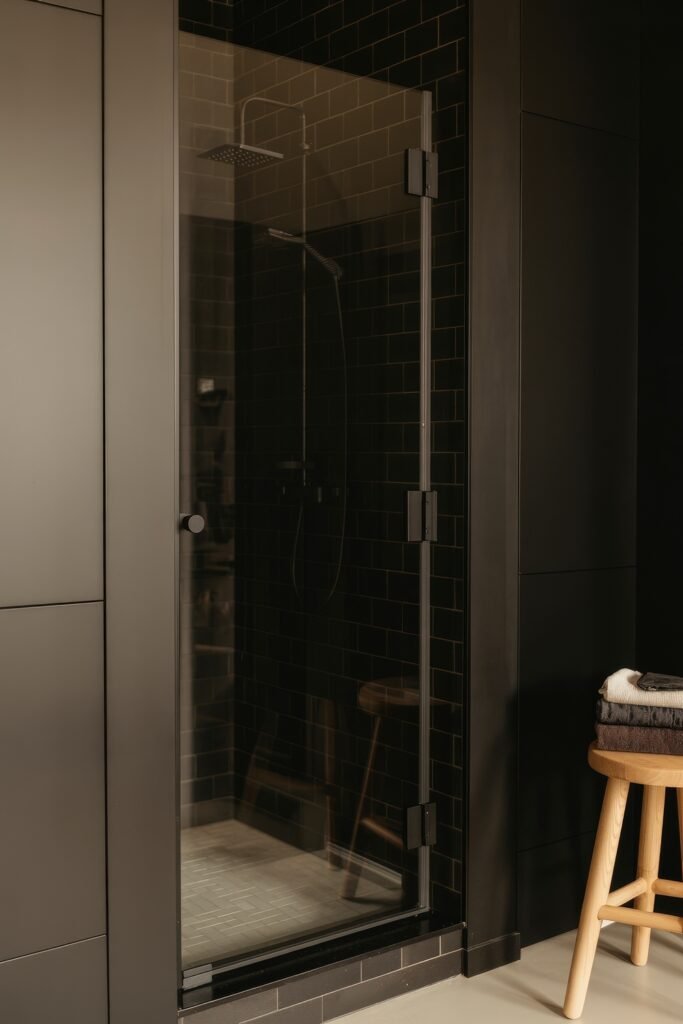 Black Bathroom Ideas: Genius Ways to Create Moody Glam 22 Dark walk-in shower with glossy black subway tiles, frameless glass door, and a wooden stool outside, capturing a minimalist and moody spa vibe.
