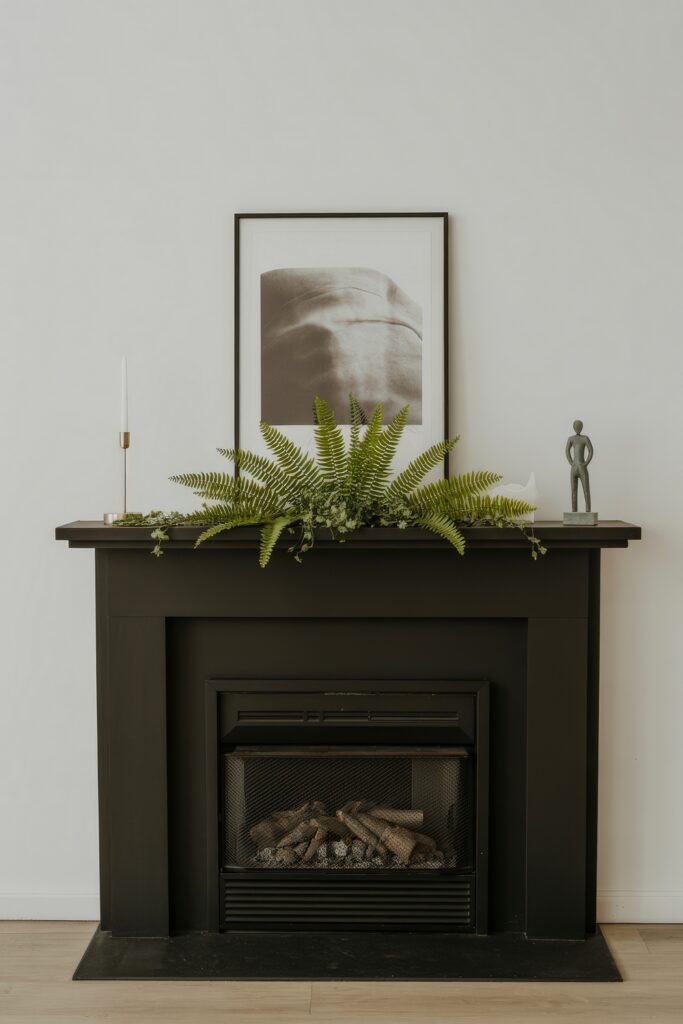 Summer Mantel Decor Tips (Even If You Don’t Have a Fireplace) 25 Black mantel with a framed art print, lush ferns, and minimal candle and sculpture accents for a modern summer décor.