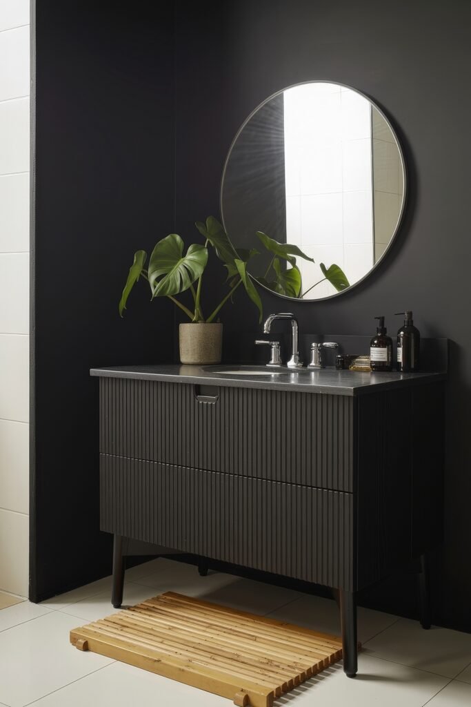 Black Bathroom Ideas: Genius Ways to Create Moody Glam 5 Black vanity with vertical grooves, chrome faucet, round mirror, and a potted monstera plant, balanced by a wooden slatted bath mat against a dark feature wall.