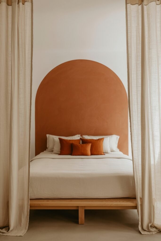 Terracotta Bedroom Ideas: Genius Ways to Glow 5 Light and airy bedroom with neutral bedding and rust-colored accent pillows, framed by sheer beige curtains and a rounded terracotta arch painted behind the bed.