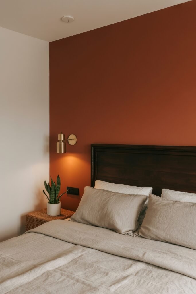 Terracotta Bedroom Ideas: Genius Ways to Glow 6 Simple bedroom with a dark wood headboard, light linen bedding, terracotta accent wall, brass wall sconce, and a small potted plant on a woven nightstand.