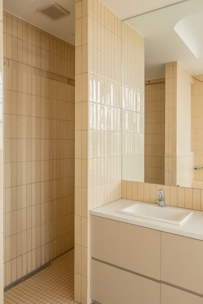 Cream Bathroom Ideas: Genius Ways to Warm Up Your Space 11 Contemporary bathroom with vertical beige tiles, a sleek vanity, and integrated mirror, creating a clean and geometric layout in a Neutral & White Bathroom Themes style.
