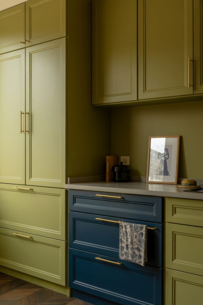Green Kitchen Cabinets: Stylish Ways to Elevate Style 11 Stylish kitchen with matte olive green cabinets and a section of navy drawers with gold handles, highlighted by minimalist decor and warm-toned lighting.