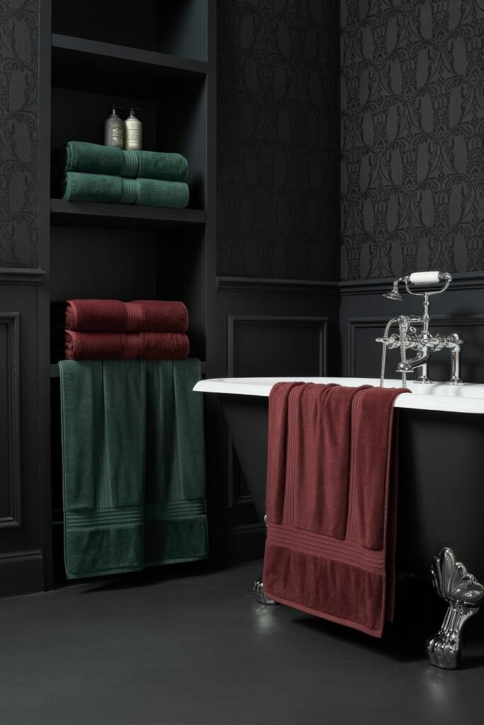 Gothic Bathroom Ideas: Genius Touches for Moody Glam 16 Elegant black bathroom with clawfoot tub and richly textured black wallpaper, accented by forest green and burgundy towels for a cozy, dramatic Gothic Bathroom Ideas feel.