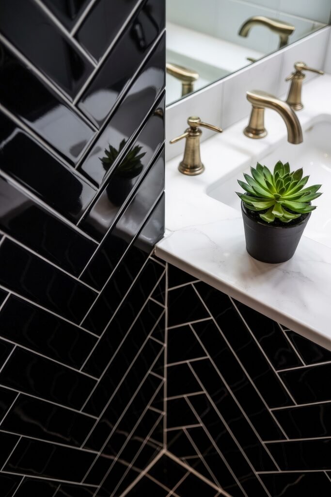 Black Bathroom Ideas: Genius Ways to Create Moody Glam 15 White countertop with brass fixtures and a green succulent in front of glossy black herringbone tiles, mixing luxe finishes with lively accents in a compact bathroom.