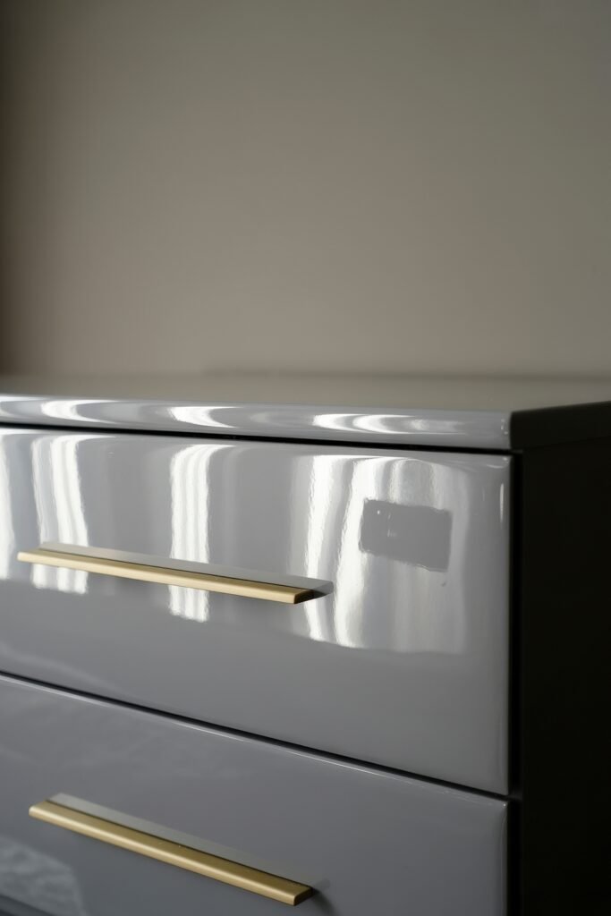 Glam Bedroom Décor: Essential Tips for Luxe Sleep 20 Minimalist glossy grey dresser with sleek gold bar handles, reflecting natural light to emphasize a clean and contemporary aesthetic.