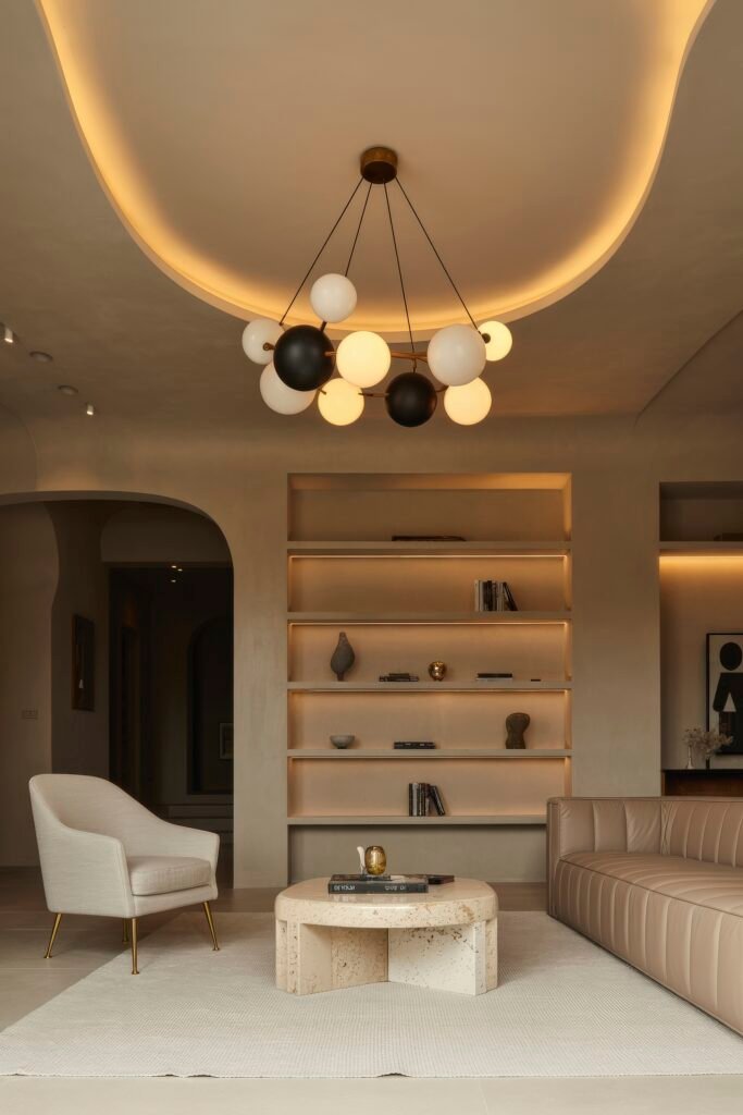 Luxury Ceiling Design in Living Rooms 5 Contemporary minimalist room with sculptural globe chandelier, built-in shelving, and a soft neutral palette highlighted by curved architectural lines and a smooth, glowing ceiling—subtle yet refined luxury ceiling design living room.