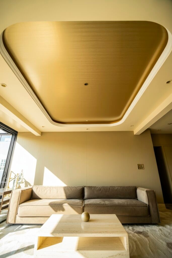 Luxury Ceiling Design in Living Rooms 18 Sunlit minimalist room with a sleek recessed ceiling in gold, neutral-toned velvet sofa, and a travertine coffee table, creating a warm and inviting luxury living room feel.