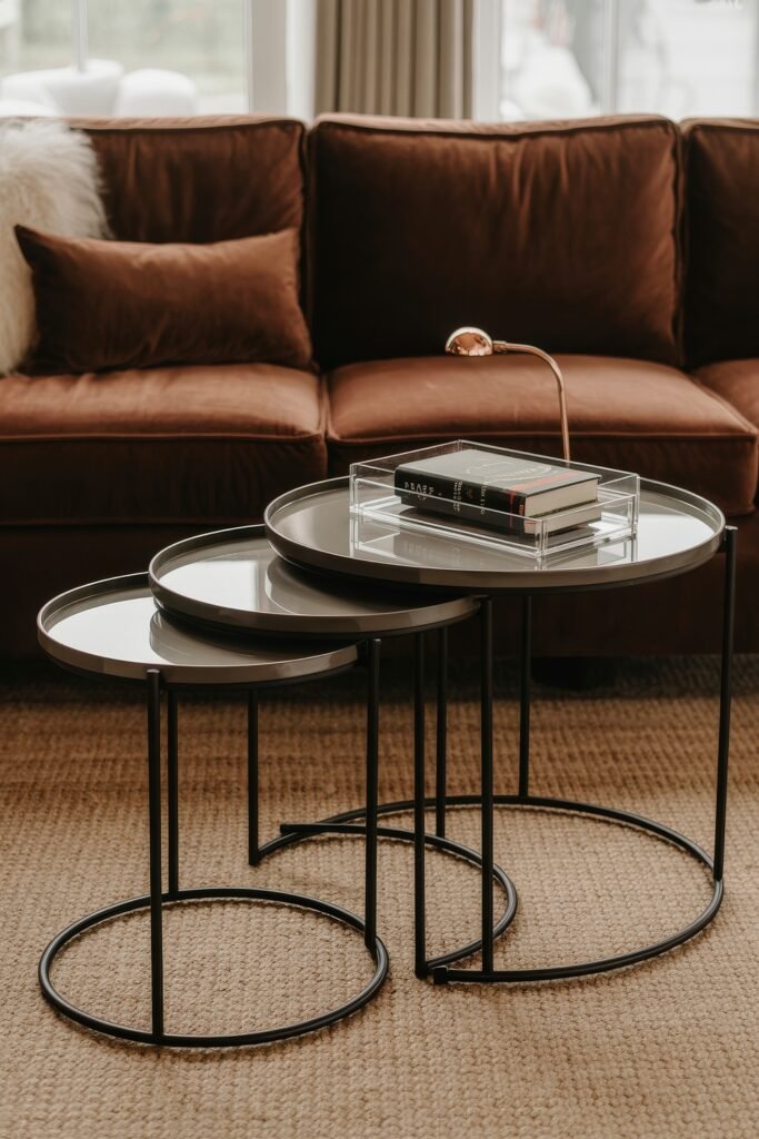 Brown Couch Living Room Ideas: Cozy and Chic Decor Inspiration 25 Rich brown couch with plush pillows beside a trio of round modern nesting tables, styled with books and a copper desk lamp for a sophisticated brown-themed setup.