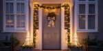 A front door decorated with a lit wreath and garland, framed by glowing Christmas lights and flanked by two illuminated cone-shaped trees, showcasing elegant christmas door decorations outdoor.