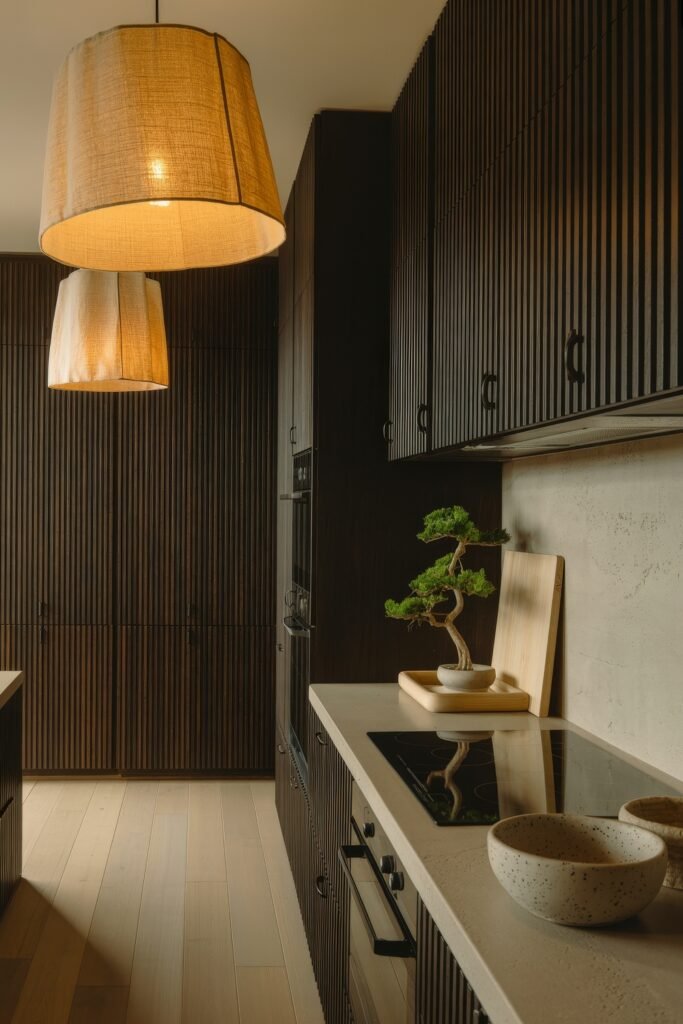 Chic Ways to Style a Modern Black Kitchen 23 Sophisticated kitchen with vertically grooved dark cabinetry, a potted bonsai, warm lighting from oversized pendants, and light wood floors for a calming zen-inspired modern black kitchen.