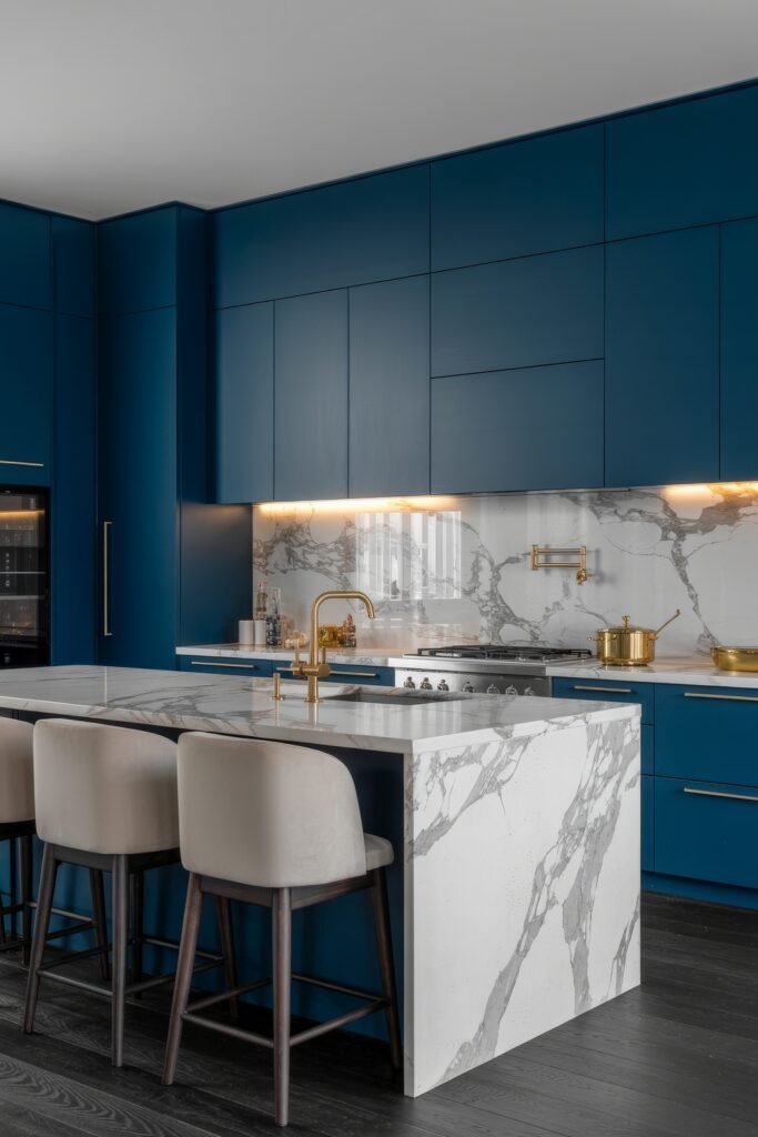Inspiring Looks for Blue Kitchen Cabinets in Every Style 31 Modern kitchen with sleek blue kitchen cabinets, a marble waterfall island, gold fixtures, and under-cabinet lighting highlighting a veined marble backsplash.