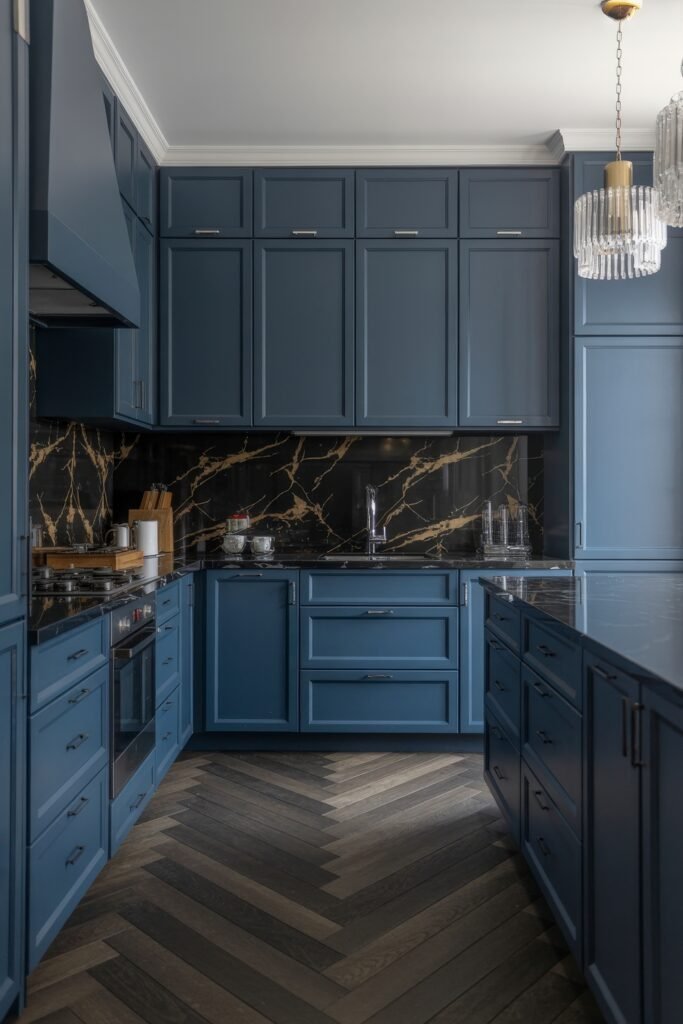 Inspiring Looks for Blue Kitchen Cabinets in Every Style 36 Contemporary kitchen with matte blue cabinetry, black marble backsplash with golden veining, chevron wood flooring, and crystal pendant lights above the island.