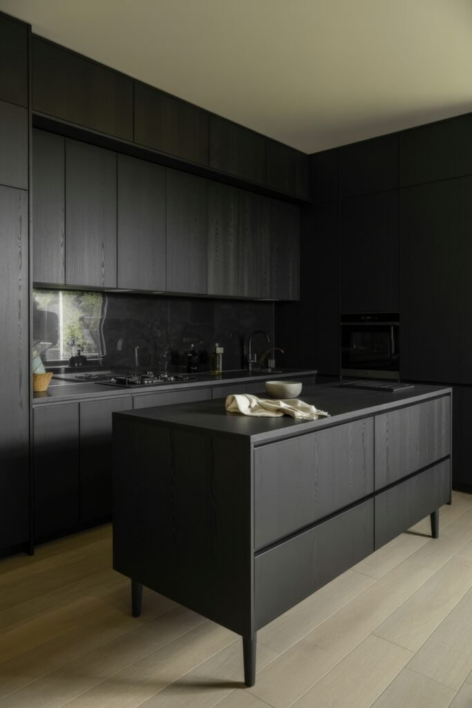 Chic Ways to Style a Modern Black Kitchen 6 Minimalist modern black kitchen with textured wood grain cabinets, a black island with matching countertop, and a high-gloss backsplash reflecting outdoor greenery.