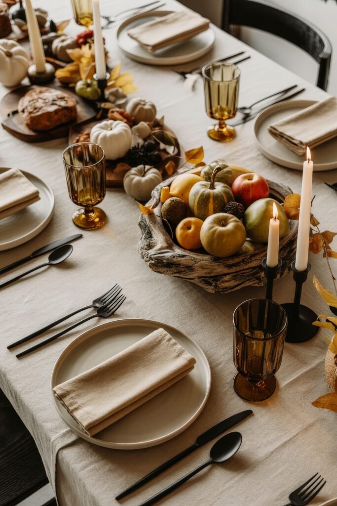 Effortless Harvest Table Looks: Thanksgiving Tablescapes Simple & Chic 11 Rustic fall table setting with a linen tablecloth, black cutlery, amber goblets, and a centerpiece of gourds, apples, bread, and mini white pumpkins in a textured wooden bowl.