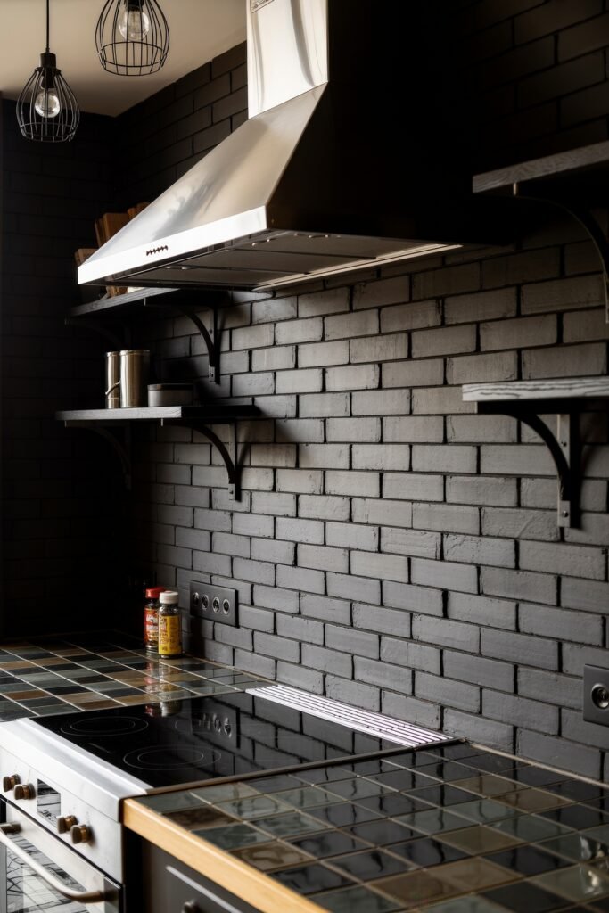 Chic Ways to Style a Modern Black Kitchen 15 Close-up of a modern black kitchen with matte brick wall, stainless steel hood, black shelving, and a dark tiled counter featuring a black glass cooktop.