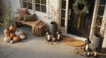 Modern fall porch with stone steps, potted greenery, glowing lanterns, and a tray of pinecones and gourds scattered among autumn leaves.
