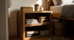 Wooden bedside shelf neatly organized with folded linens, stacked books, and small decorative items, offering practical storage ideas for small bedrooms.