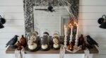 Rustic mantel decorated with faux cobwebs, black crow figurines, amber glass bottles, pillar candles, and cloche-covered white pumpkins for farmhouse Halloween home décor.