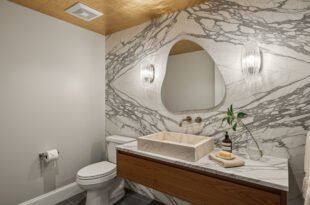 Modern half bathroom with a marble accent wall, floating wood vanity, vessel sink, and abstract mirror framed by two wall sconces.