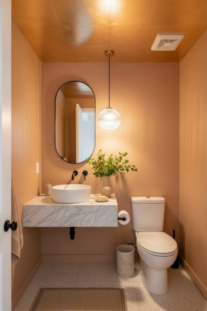 Half Bathroom Decor, Elevated: Jewel-Box Ideas 17 Cozy half bathroom with peach-toned walls, marble floating vanity, round mirror, and pendant light.