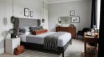 Effortlessly Stylish bedroom ideas for men That Feel Personal Sophisticated bedroom with a gray upholstered headboard, layered bedding, warm wood furniture, and modern lighting, offering refined bedroom ideas for men.