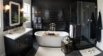 Fresh Ideas for Black and White Bathroom Decor Stylish black and white bathroom decor featuring glossy black subway tiles, a freestanding white tub with a wooden tray, a glass-enclosed shower, and a sleek black vanity with a white countertop.