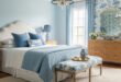 Fresh blue bedroom ideas for a calm, chic retreat 259 Elegant bedroom with light blue walls, white upholstered headboard, patterned bench, and layered blue bedding accented by striped lamps and wicker furniture.