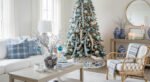Bright living room with a Christmas tree decorated in blue and silver ornaments, paired with cozy white seating and blue plaid pillows for an elegant blue Christmas décor theme.