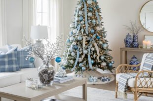 Bright living room with a Christmas tree decorated in blue and silver ornaments, paired with cozy white seating and blue plaid pillows for an elegant blue Christmas décor theme.
