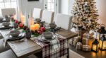 Cozy Ways to Style Farmhouse Christmas Décor Rustic dining room set with gray dishware, plaid table runner, candles, pinecones, and pomegranates, styled beside a glowing Christmas tree and farmhouse-style wrapped gifts.