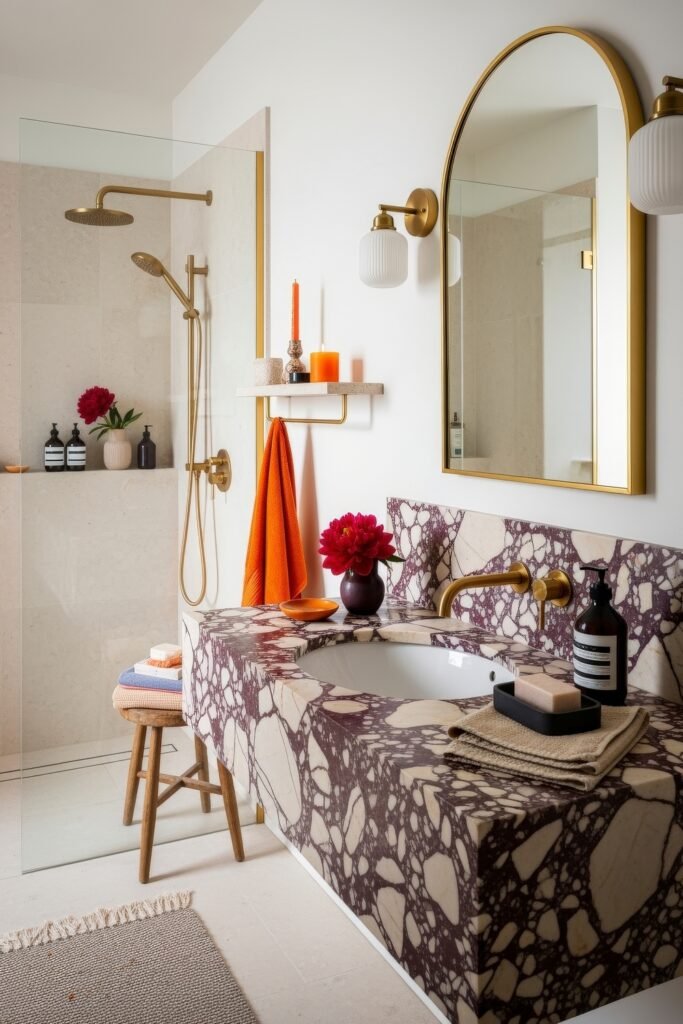 Bathroom Decor Inspo: Fresh Ideas for gold bathroom decor 22 Contemporary bathroom featuring bold marble vanity, arched mirror with gold frame, gold shower fixtures, and pops of orange decor with fresh flowers.