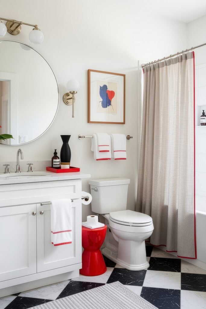 13 Bold Ideas for Red Bathroom Decor That Wow 5 White bathroom with black-and-white tile floor, red stool, and red-trimmed towels, accented by a large round mirror and framed art.
