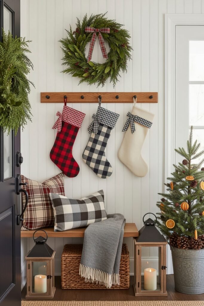 Cozy Ways to Style Farmhouse Christmas Décor 10 Charming holiday entryway featuring plaid stockings and pillows, greenery wreath with red bow, lanterns with candles, and a small Christmas tree decorated with dried orange slices.