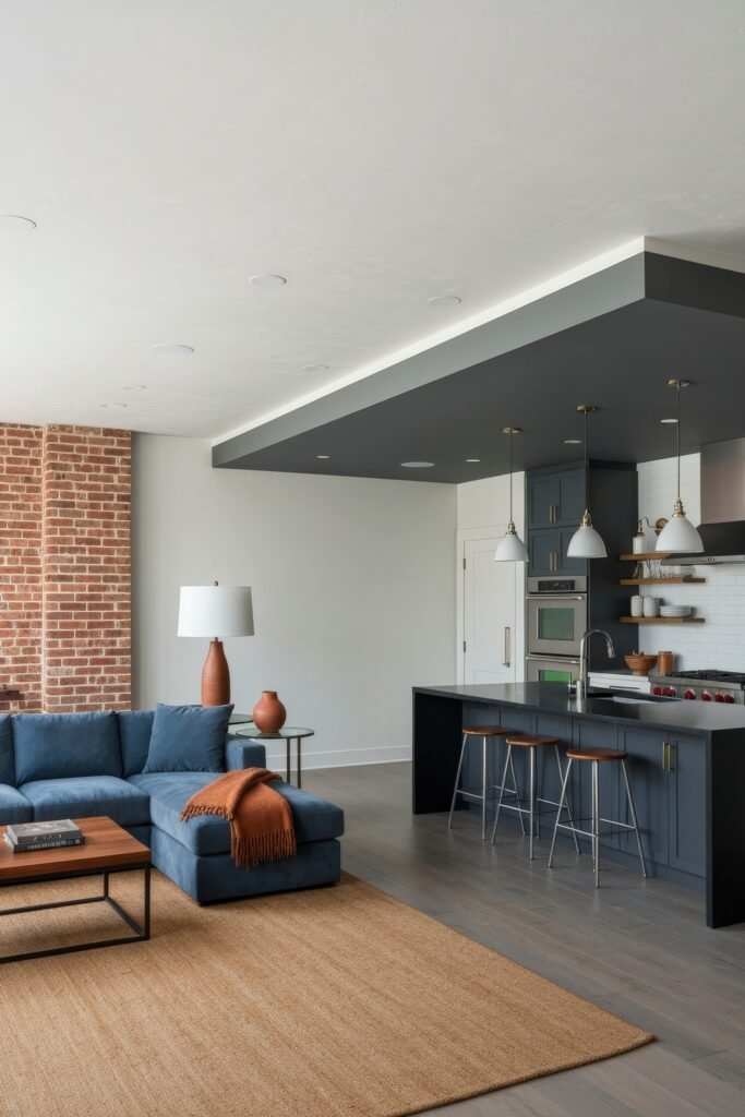 Smart Ways to Style a Kitchen and Living Room Combo 11 Contemporary kitchen and living room combo with navy blue cabinetry, exposed brick, and a matching sectional sofa, accented by warm wood tones, pendant lights, and minimalist styling.