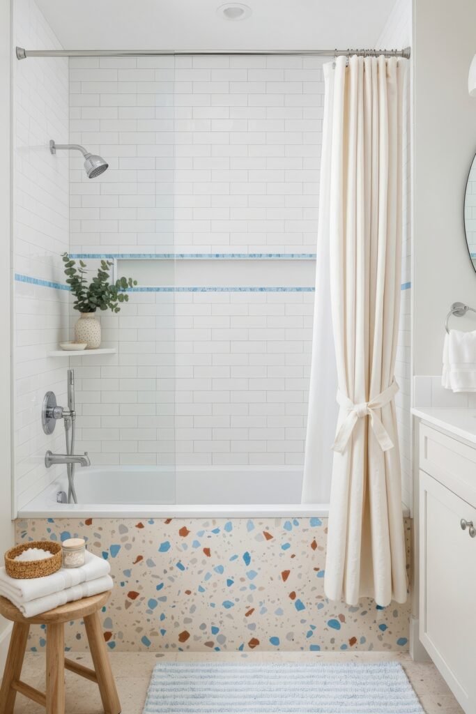Fresh, Stylish Ways To Elevate Your Tub Shower Combo 12 Bright bathroom with terrazzo tub front, white subway tile walls accented with blue stripes, chrome fixtures, and a white curtain tied to the side.