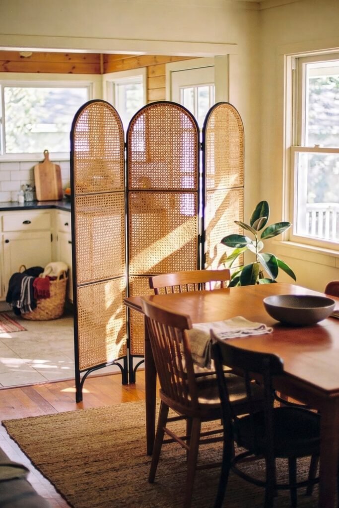 Kitchen Dining Room Combo Ideas That Feel Effortless 23 Cozy and sunlit kitchen dining room combo with a wooden table, mixed dining chairs, and a rattan room divider that separates the cooking area, enhancing warmth and privacy in the open-plan space.