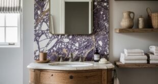 Rustic bathroom vanity with curved wood cabinet and marble sink beneath a Calacatta Viola stone accent wall and open shelves with pottery and towels