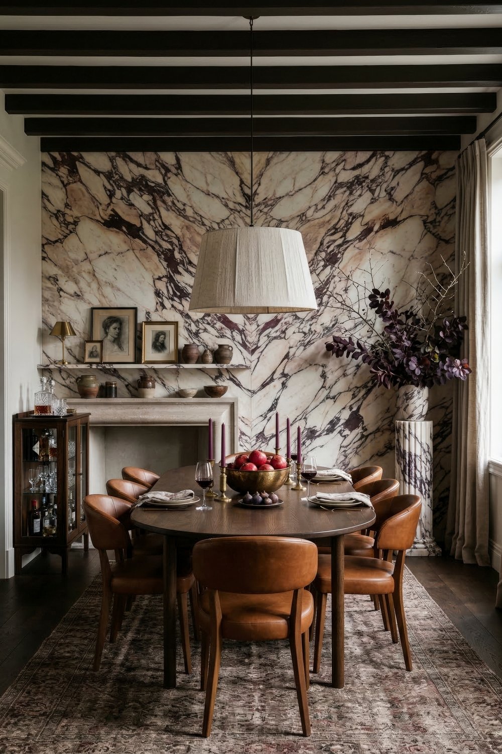 Elegant dining room with a round wood table and leather chairs beneath a large pendant against a dramatic bookmatched marble wall