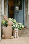 Easter Front Porch Ideas for a Fresh Spring Entry Woven bunny porch decor beside baskets of white tulips and hydrangeas at a blue front door