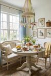 Cottage breakfast nook with pastel ribbon chandelier spring flowers painted eggs cake and tulips beside large windows and vintage botanical wall art